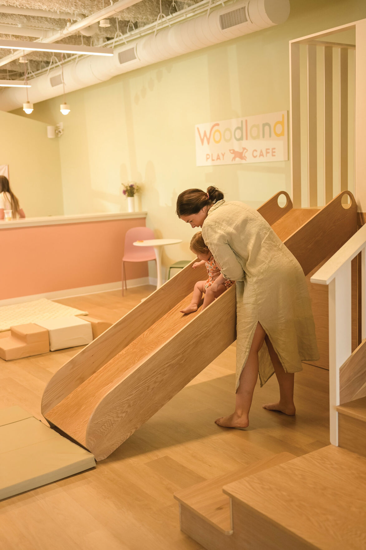 A mother places her child on a slide inside of Woodland Play Cafe